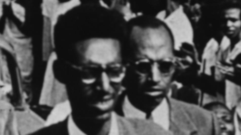 King Kigeli V of Rwanda (front) is flanked by guards and crowds as he is escorted through a town, circa 1959.
