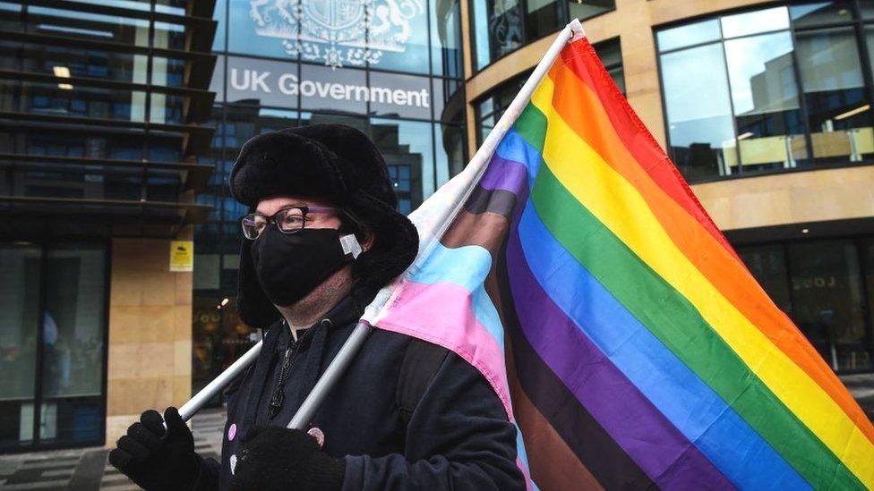 A person holds a rainbow-coloured flag