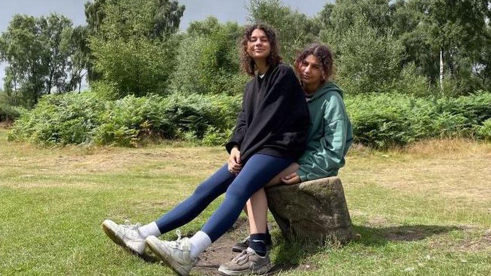 A girl sits on a tree stump with her twin sister on her lap