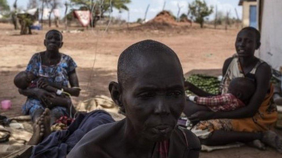 A cholera-stricken woman showing signs of malnutrition sits next to fellow patients (background) outside a temporary field hospital near the remote village of Dor in the Awerial county in south-central Sudan on April 28, 2017