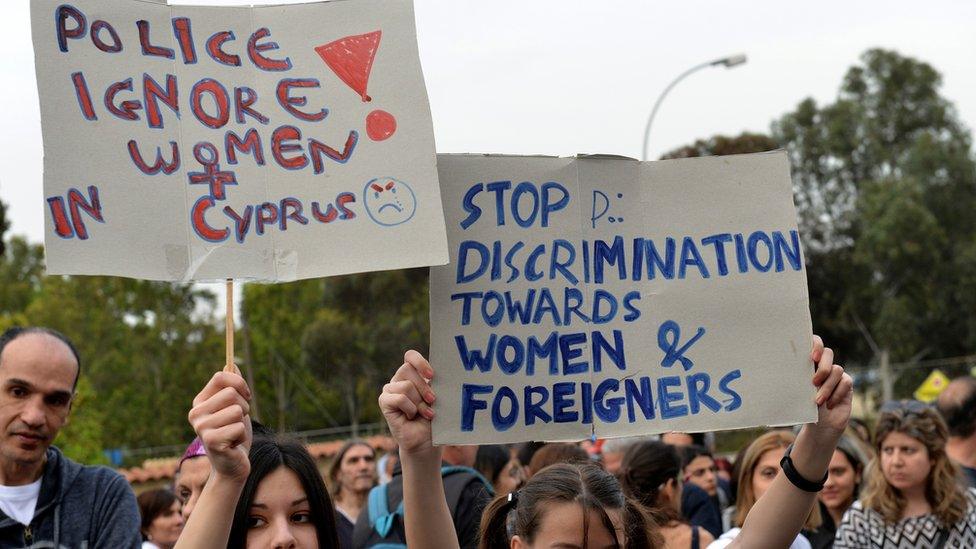 Protestors holding up signs saying "Police ignore women" and "stop discrimination towards women and foreigners"