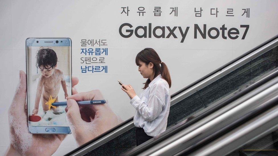 A woman looks at her mobile phone as she rides an escalator past an advertisement for Samsung's Galaxy Note 7 device at a Samsung store in Seoul