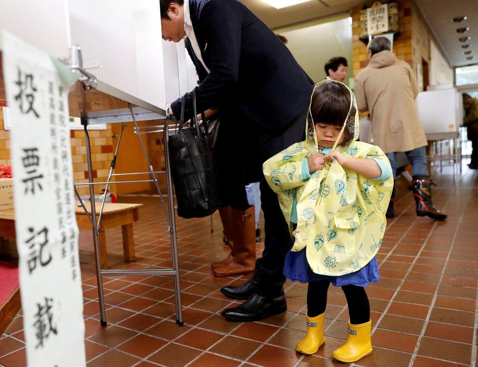 A girl stands next to her father filling out his ballot for a national election at a polling station in Tokyo, Japan October 22, 2017