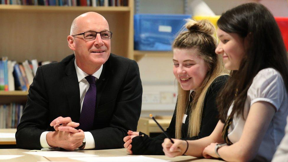 John Swinney sitting talking to pupils in a classroom