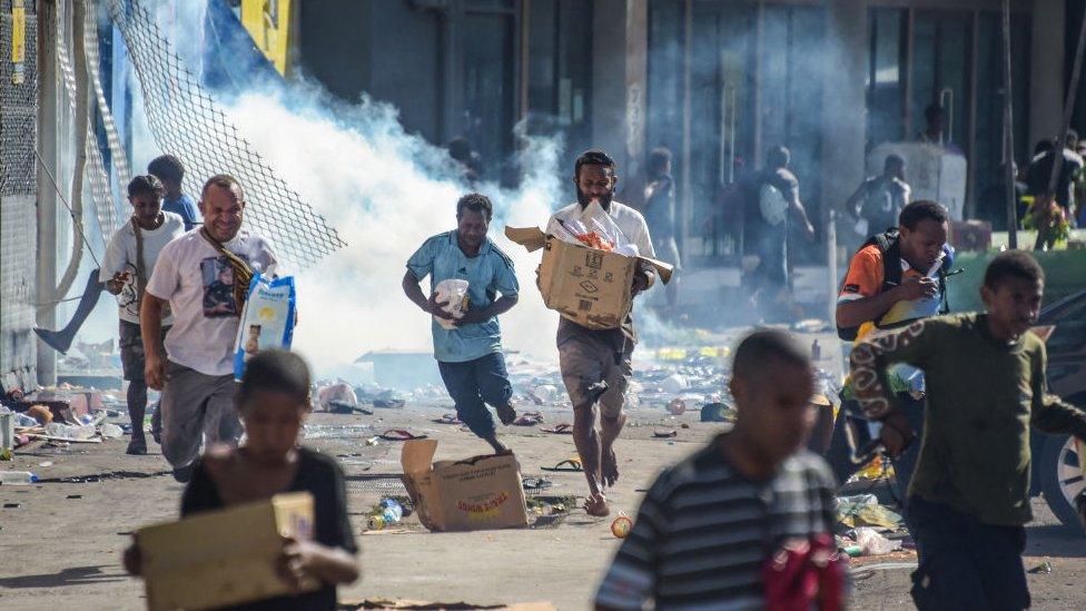 People run with merchandise as crowds leave shops with looted goods amid a state of unrest in Port Moresby on January 10, 2024