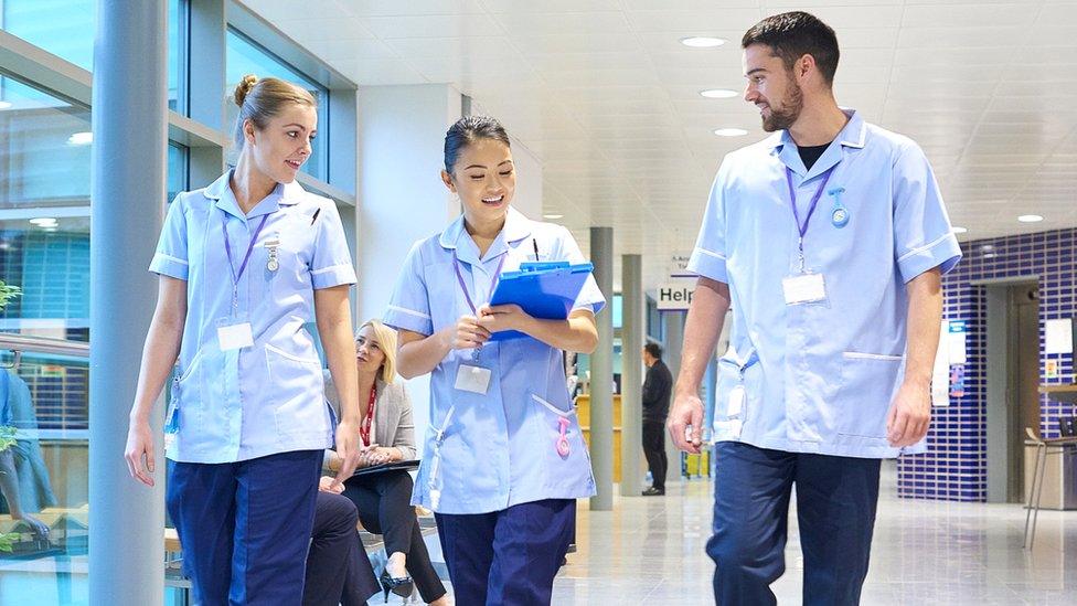 Three nurses walk along a corridor in a hospital.