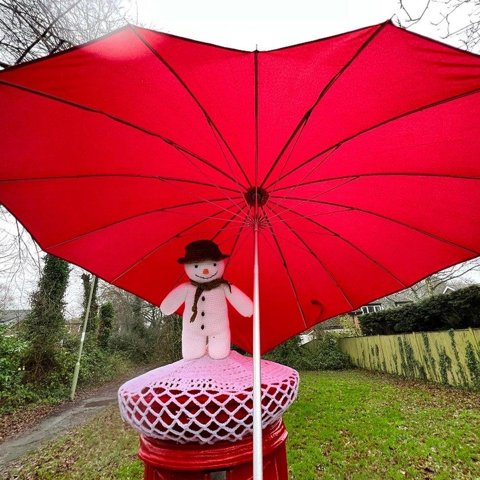 A snowman post box topper with a red umbrella