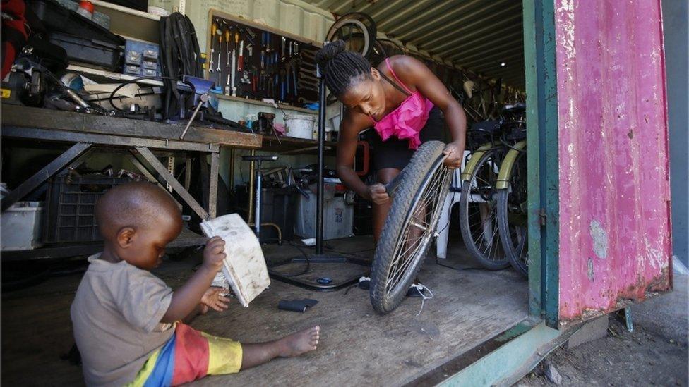 One and a half year old Tishe Mlambo plays whilst his mother, 23-year-old bicycle mechanic Rumbidzai Mlambo, repairs a puncture on a bicycle in a converted shipping container workshop that is the Bicycling Empowerment Network (BEN) centre in Masiphumelele, Cape Town, South Africa, 11 April 2011