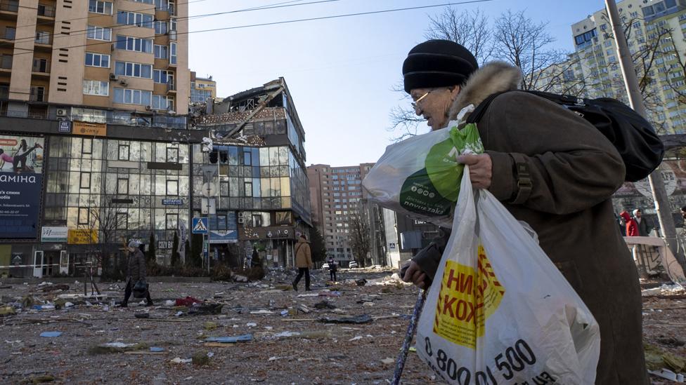 A woman walks past a damaged building following the curfew being temporarily lifted