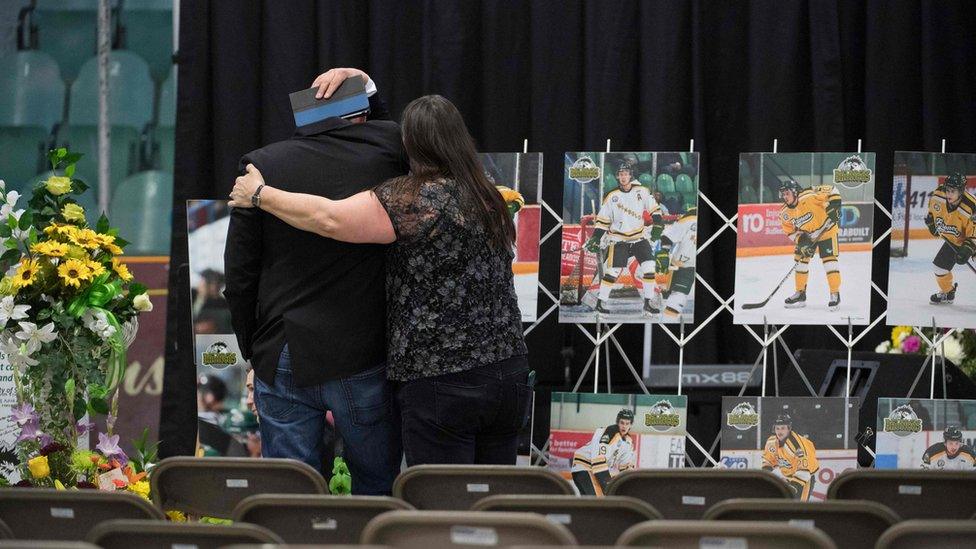 A man is comforted as he looks at photographs prior to a vigil at the Elgar Petersen Arena, home of the Humboldt Broncos