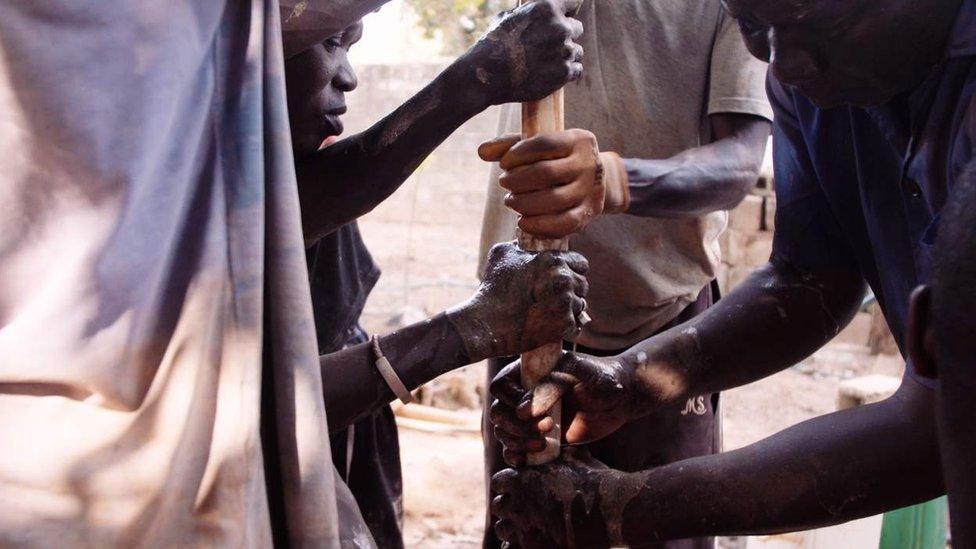 People grouped around and holding a pipe as part of making a borehole.