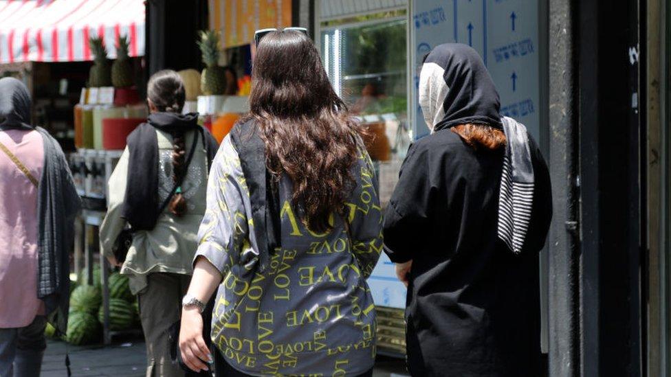 Two women walk down a street in Iran without their hair covered