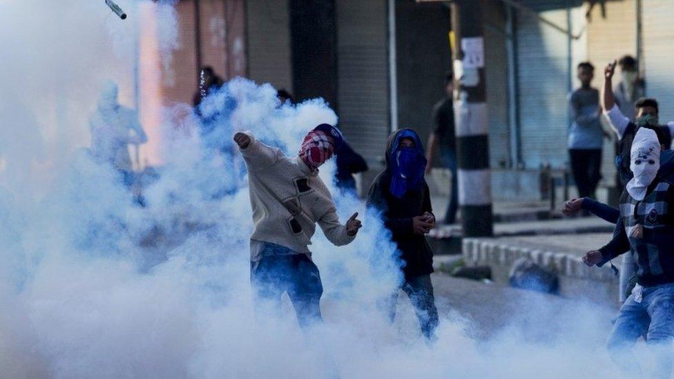 A Kashmiri masked Muslim protester throws back an exploded tear gas shell at Indian policemen during a protest in Srinagar, Indian controlled Kashmir, Tuesday, April 12, 2016.