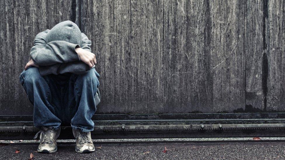 Young person crouched up against a wall