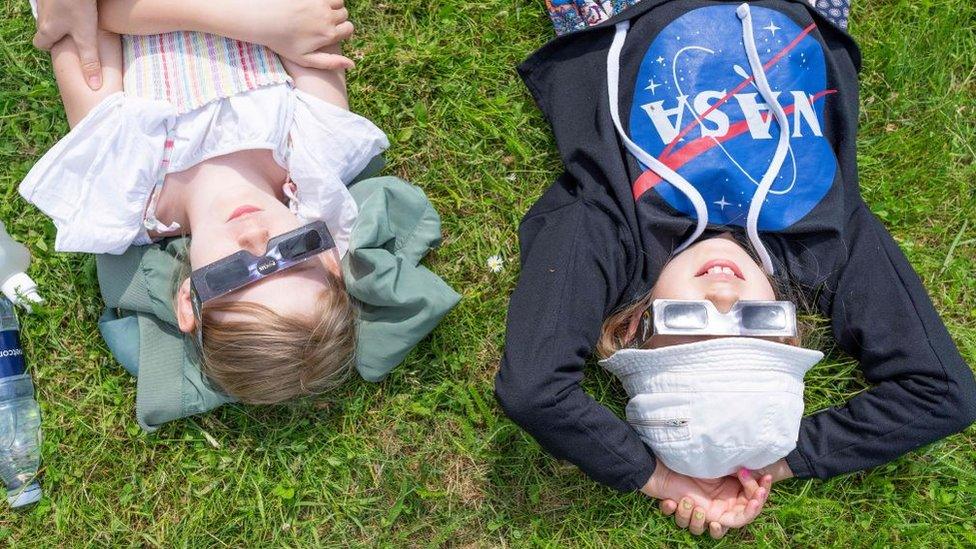 Children lie on the lawn and look through glasses waiting for the partial solar eclipse.