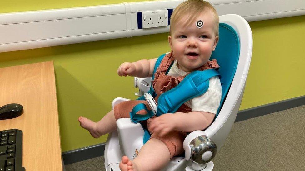 A baby sits in a chair with a sticker on her forehead