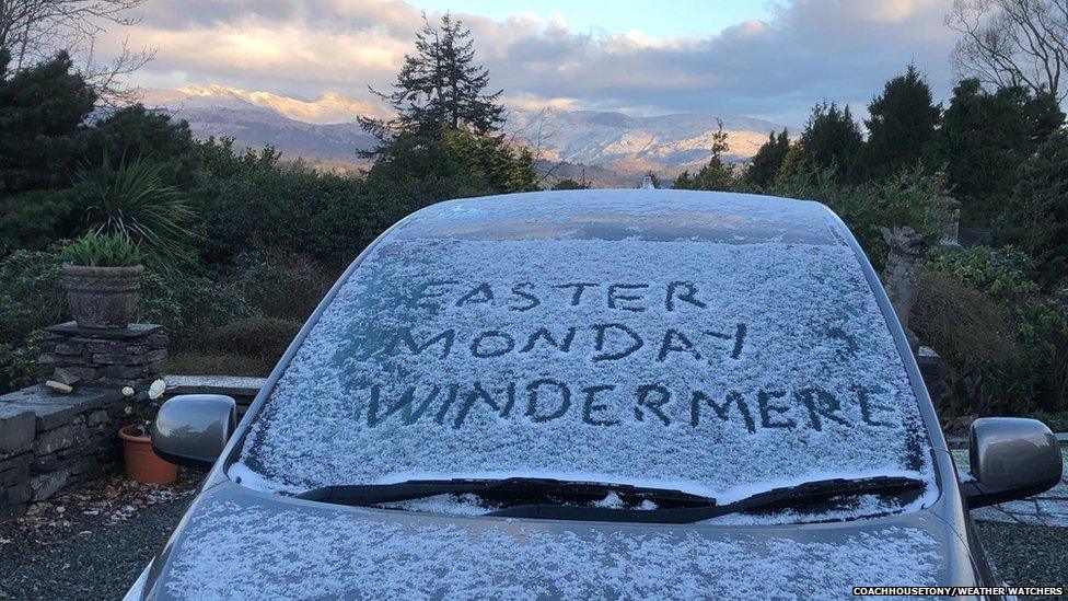 "Easter Monday Windermere" written on the windscreen on a frost-covered car with cloud-topped hills in the background