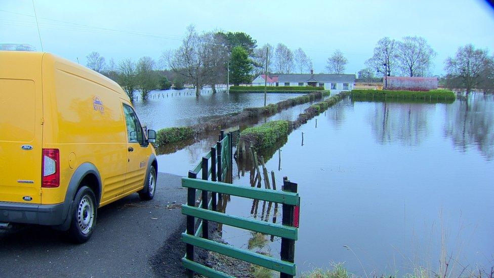 A Rivers Agency van sits at the end of a lane to a house surrounded by flooded fields