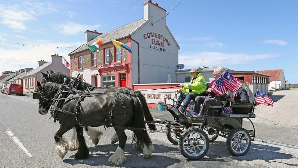 Horses leading a cart carrying people holding American flags