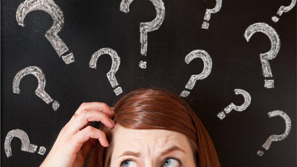 Woman scratching her head in front of question marks