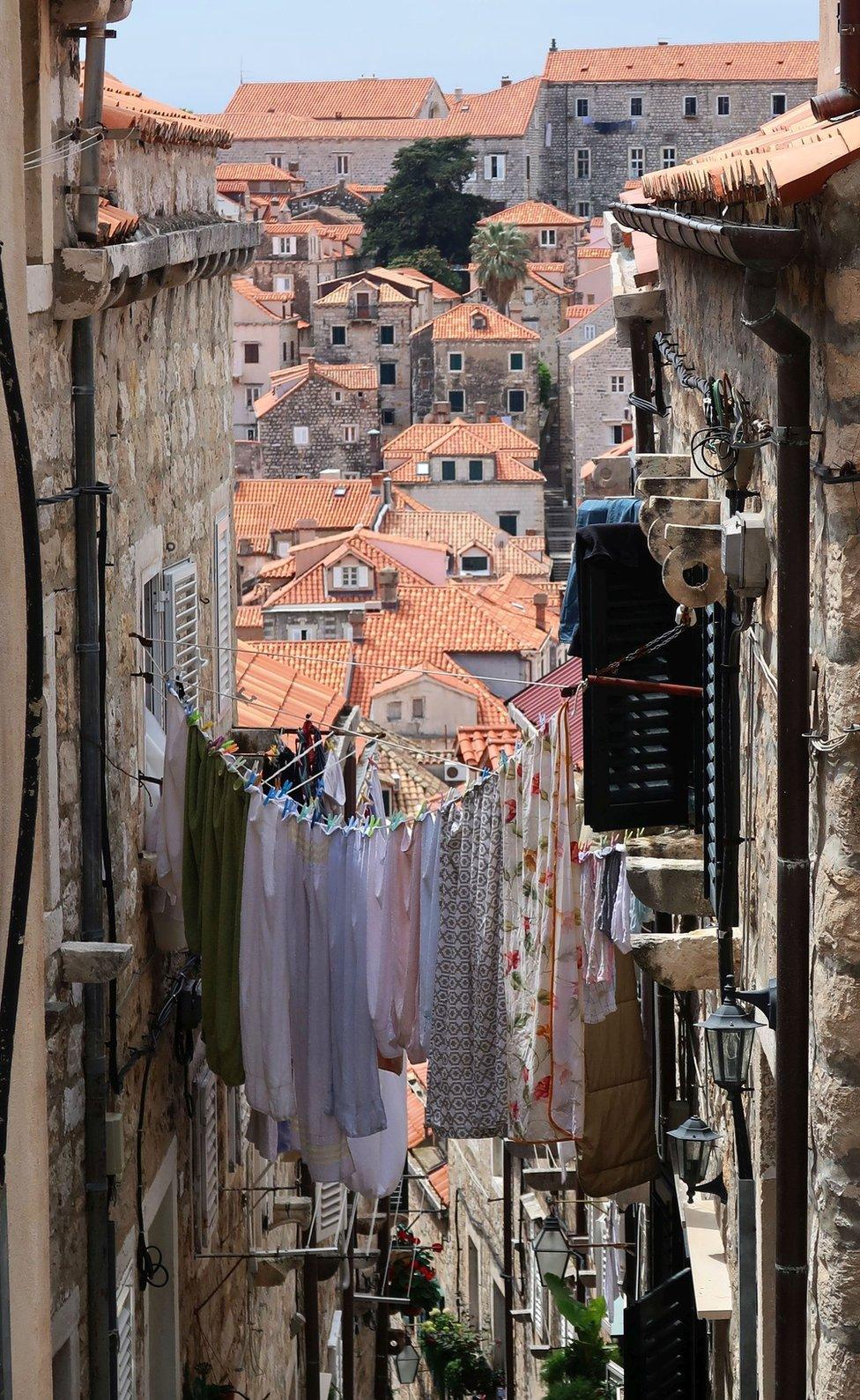 A narrow street connected by a washing line full of clothes over looks a town in the distance