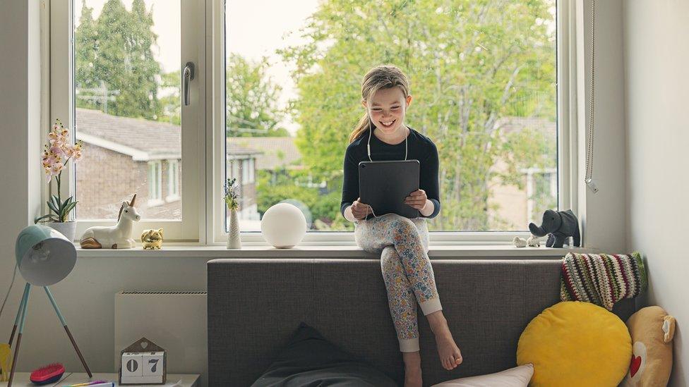 girl sat on window sill holding ipad smiling