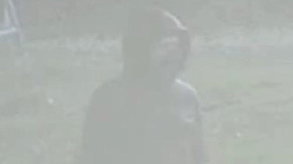 A blurred CCTV image of a man in a hooded jacket and facemask