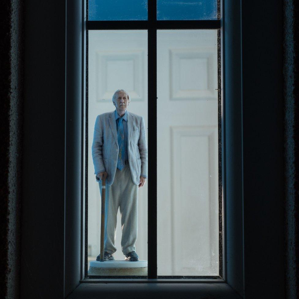 A man stands looking out of a window