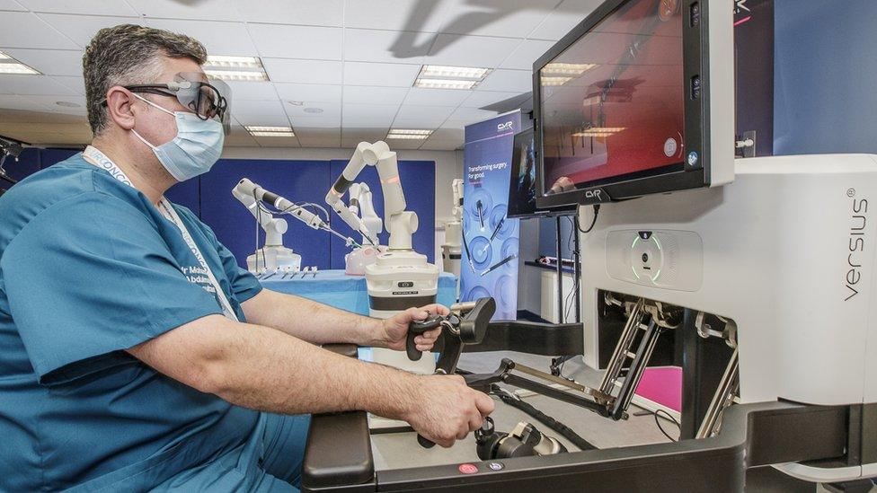 Consultant urologist Mohamed Abdulmajed at the controls of the surgical robot, which is operating in the background behind him