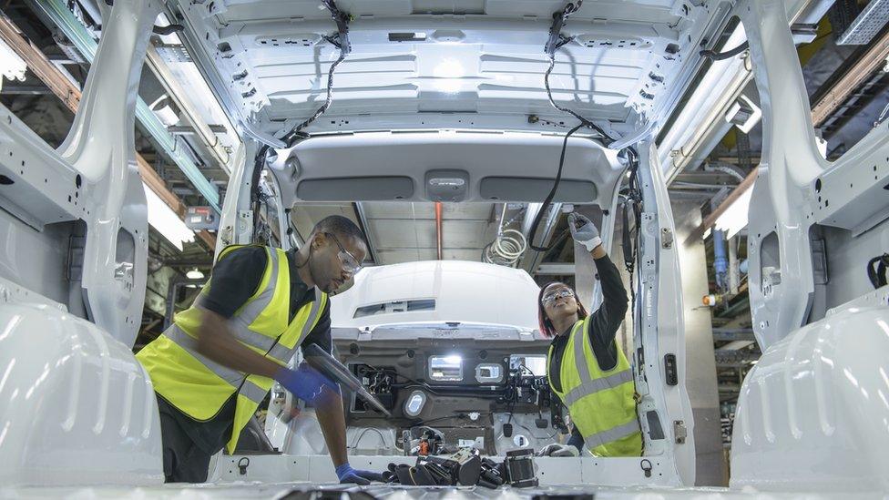 Car workers wearing high visibility jackets fitting parts on vehicle on production line in car factory