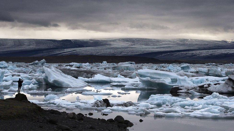 A man takes a picture of blue icebergs at the Jokulsarlon glacial lagoon