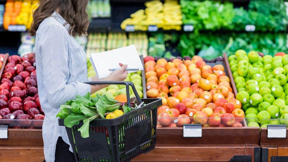 Woman carries a shopping basket filled with fresh produce, buying fresh fruit and vegetables in a supermarket or grocery store