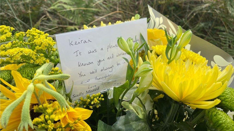 Floral tribute with note attached at site of crash