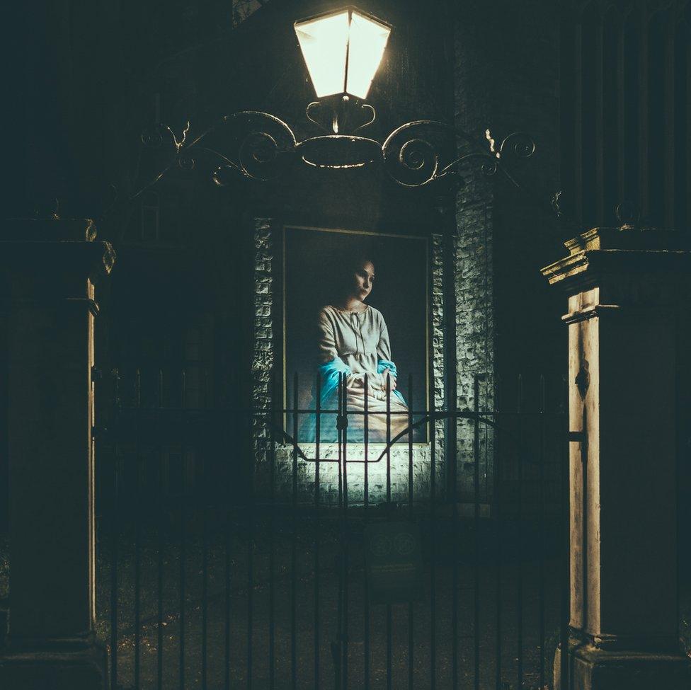 An image of a portrait of a woman looking thoughtful on a wall behind a gate