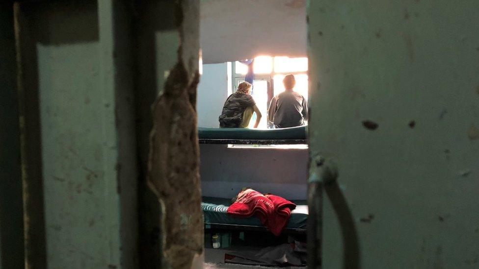 Two boys sit on a bunkbed in a cell