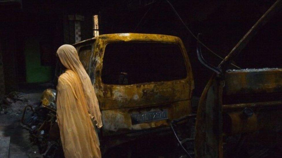 A Muslim woman looks at a burnt vehicle