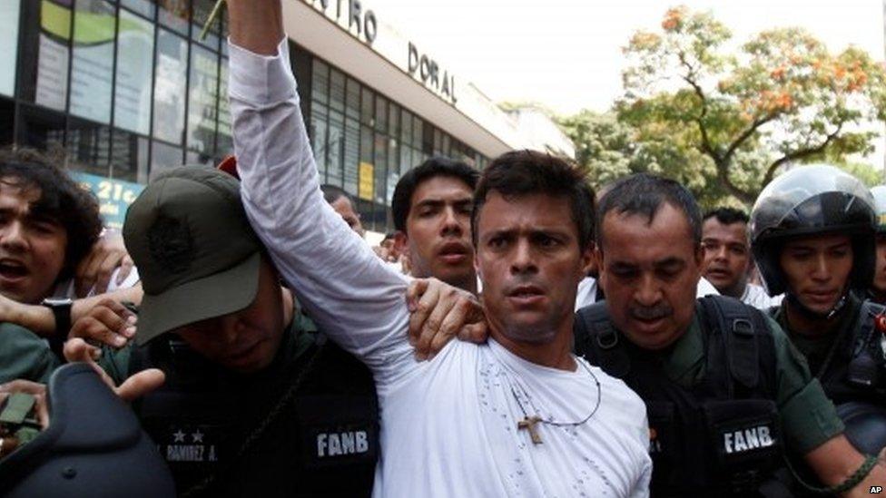 In this Feb. 18, 2014 file photo, opposition leader Leopoldo Lopez, dressed in white and holding up a flower stem, is taken into custody by Bolivarian National Guards, in Caracas, Venezuela.