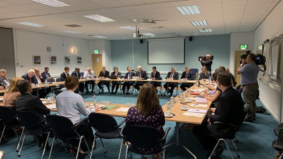 Over 20 taskforce members holding a meeting around a set of tables