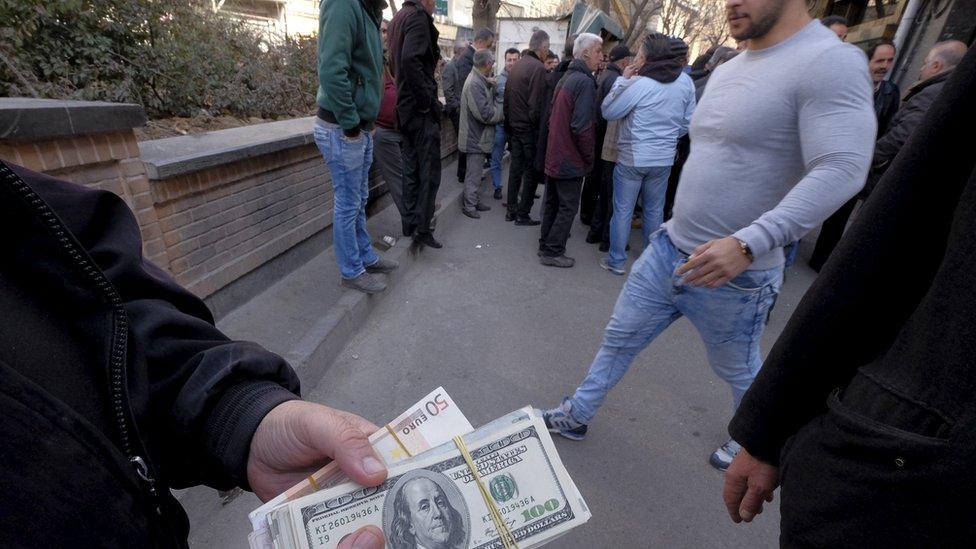 A money changer holds US dollar banknotes as he waits for customers in Tehran's business district, Iran, 17 January