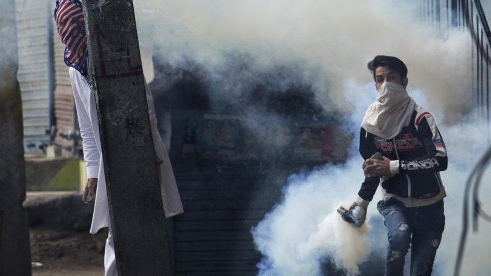 A Kashmiri Muslim protester prepares to throw back a tear gas canister at Indian security personnel as another takes cover behind an electric pole during a protest after Eid al-Adha prayers in Srinagar, Indian controlled Kashmir, Tuesday, Sept. 13, 2016