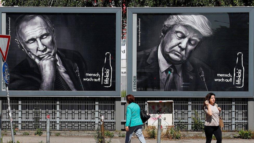 People walk past advertising posters of a German soft drink producer depicting Russian President Vladimir Putin and U.S. President Donald Trump during the G20 summit in Hamburg, Germany, 6 July 2017.