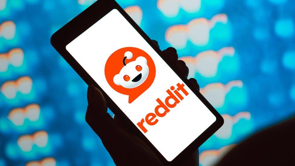 A hand holding a phone with the Reddit logo on it