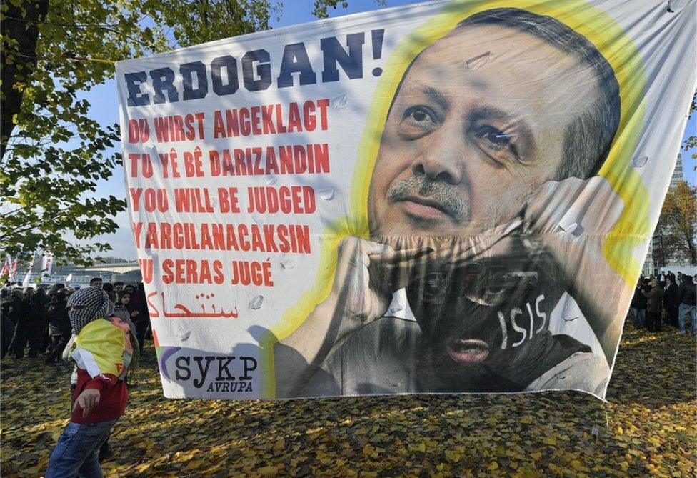 A banner shows an Islamic State group militant unmasked as Turkish president Recep Tayyip Erdogan, reading "You will be judged" during a protest in Cologne, Germany on November 12, 2016.