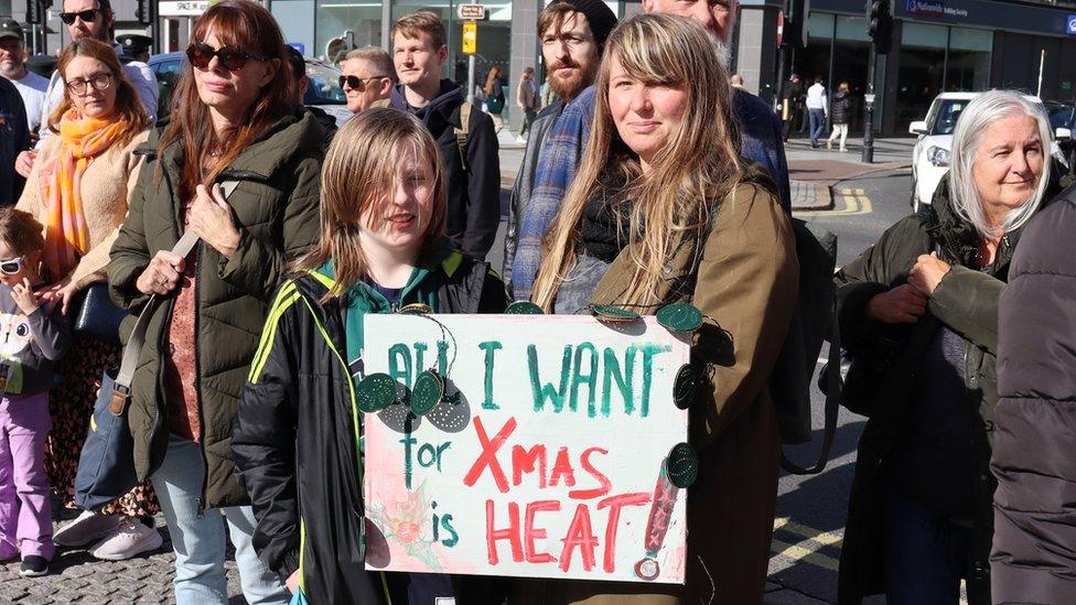 A mother and a son hold a sign that reads: All I want for Xmas is heat