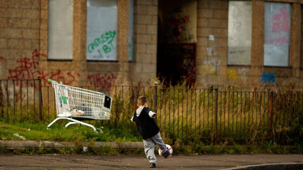 Child playing next to boarded-up houses in Govan