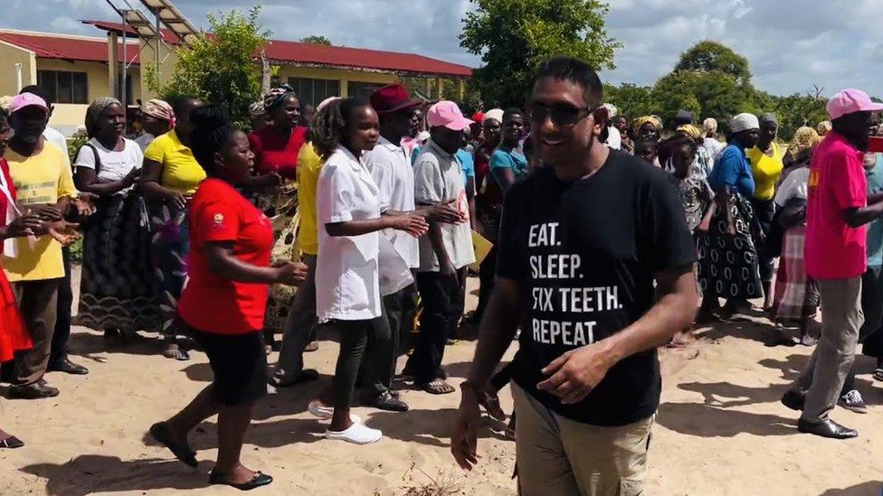 Dr Vivak Shah stands amid a crowd of people as he sets up camp to treat patients