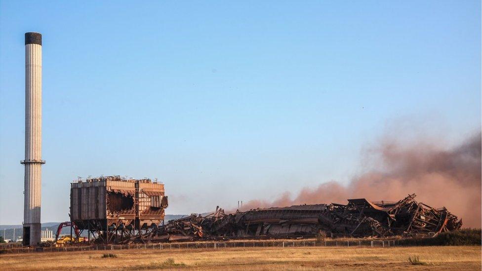 A tall chimney and two metal structures stand next to the collapsed building