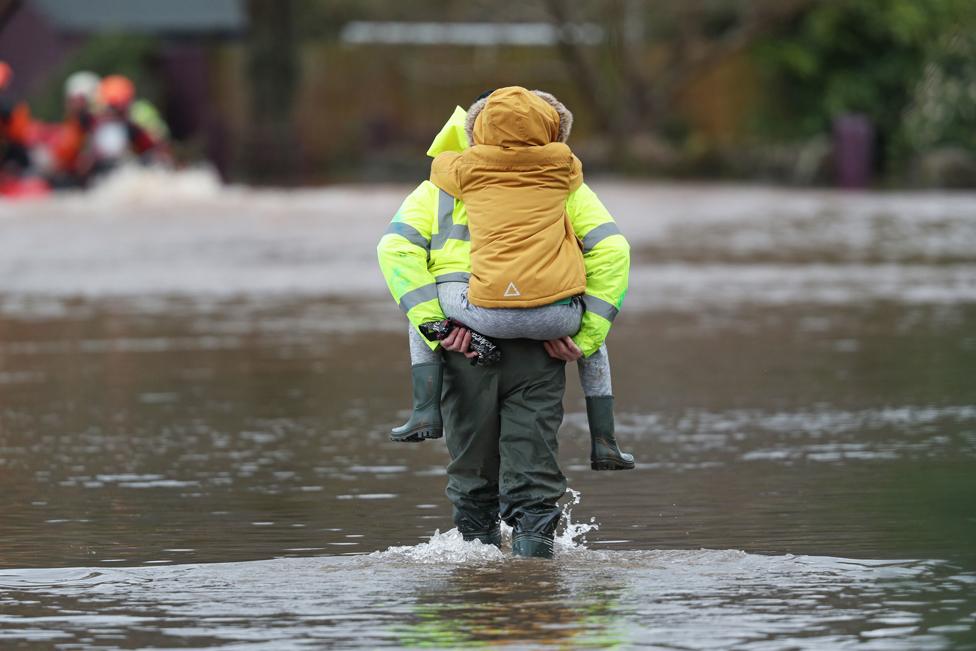 A man carries a child through floodwater in the village of Whitchurch in Herefordshire