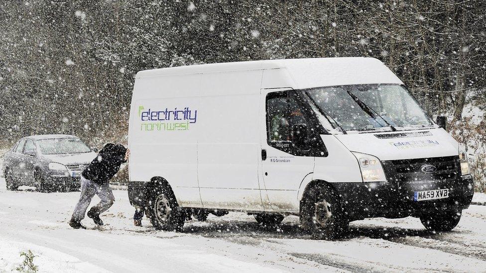 A man tries to push a van uphill on a snow-covered road