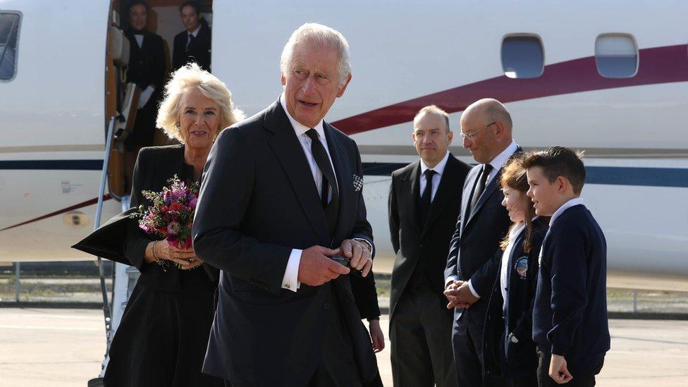 King Charles and Camilla carry gifts they received after being greeted on their arrival at Belfast City Airport